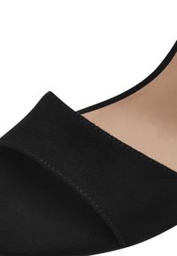 Black suede open-toe heel with a wide strap, smooth inner lining, and stitched detailing along the edges. The design is minimalistic.