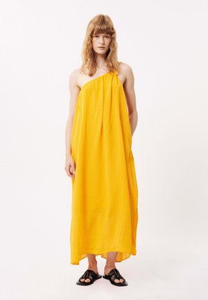 Robe maxi sans manches jaune en tissu léger, présentant un motif texturé et un ourlet asymétrique, associée à des sandales noires.
