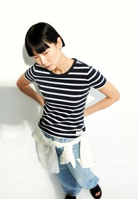 Camiseta de rayas azul marino y blanca de manga corta con textura acanalada, combinada con jeans relajados de color azul claro y una camiseta blanca atada a la cintura.