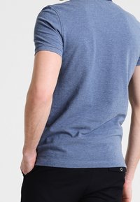 Kortärmad blå pikétröja i mjukt tyg med en kroppsnära passform och rund halsringning. Platta sömmar och en liten logotyp pryder baksidan.