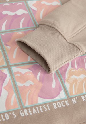 Beige sweatshirtmanchet hviler på et grafisk tryk med farverige læber i pink og fersken nuancer, med hvide detaljer og fed tekst under.
