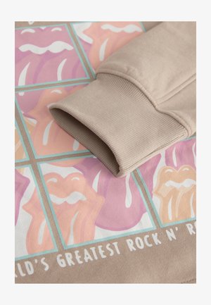 Smėlio spalvos džemperio rankogalis ilsisi ant grafikinio atspaudo, kuriame pavaizduotos spalvingos lūpos rožinės ir persikinės spalvos tonų, su baltais akcentais ir ryškiu tekstu apačioje.