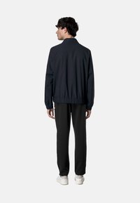 Giacca leggera di un blu navy scuro con vita elastica, vestibilità leggermente ampia e maniche lunghe; abbinata a pantaloni neri e sneakers bianche.