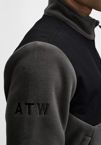 Kurtka polarowa z czarnym materiałem i szarymi rękawami z polaru. Posiada wysoki kołnierz oraz haft "ATW" na ramieniu. Miękka tekstura, nowoczesny design.