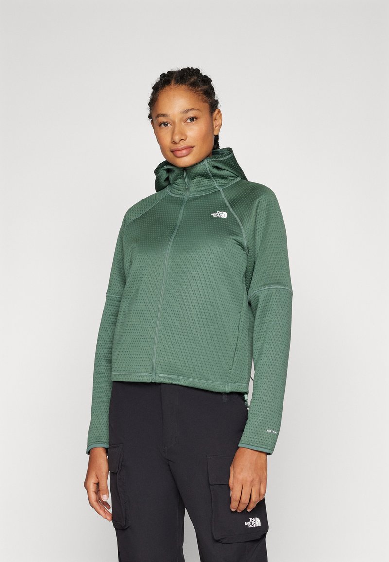 Grønn zip-up hettegenser med teksturert stoff, justerbar hette og logo på brystet. Kombinert med svarte cargo-bukser med sidelommer.