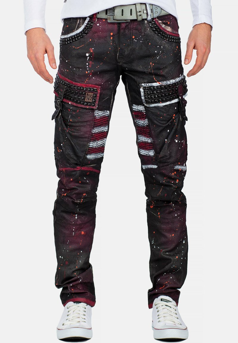 Zwarte cargo broeken met meerkleurige verfspray, textuurstof, versieringen op de zakken en ribbelpatronen. Gecombineerd met witte sneakers.