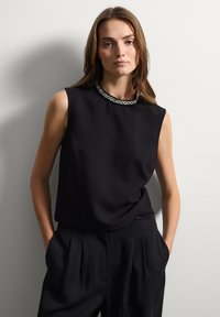 Top negro sin mangas con un escote redondeado que presenta un ribete decorativo de cuentas plateadas, combinado con pantalones negros de corte holgado.