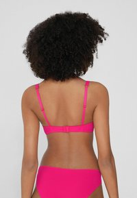 Růžový bikinový top s nastavitelnými ramínky a zapínáním na háček vzadu, doplněný o odpovídající bikinové kalhotky. Hladká textura, jednoduchý design.