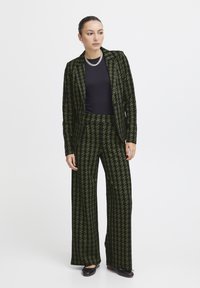 Roheline houndstooth mustriga bleiser ja laiad püksid, valmistatud tekstuuriga kangast, koos musta toppi ja tumedate kingadega. Hõbedane kettkaelakee kuulub komplekti.