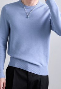 Light blue knitted sweater with a textured surface, crew neckline, and ribbed cuffs and hem. Worn over black pants.