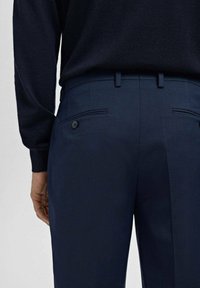 Granatowe spodnie z teksturowanym wzorem, z tylnymi kieszeniami i guzikiem, zestawione z ciemnym topem z długim rękawem.