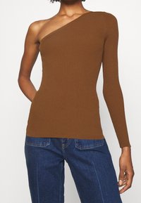 Asymetrický hnědý žebrovaný top s jedním dlouhým rukávem a jedním odhaleným ramenem, vyrobený z elastického materiálu. Má přiléhavý střih.