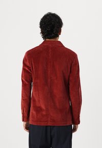 Röd kordjacka med en strukturerad design, synlig ribbad textur och en standardkrage. Har långa ärmar och en rak fåll.
