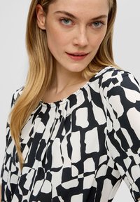 Zwart-wit gebloemde blouse van zachte stof, met ronde halslijn en plooidetail. Kenmerkt abstracte vormen en een vloeiende uitstraling.