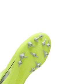 Suela de bota de fútbol en un amarillo brillante con clavos plateados. Superficie texturizada con surcos prominentes para tracción. Diseño elegante y curvado.