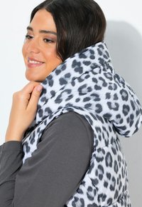 Gilet imbottito in stampa leopardata con cappuccio alto, caratterizzato da colori bianco e grigio. Il corpo è trapuntato e il design presenta una texture di tessuto liscia.