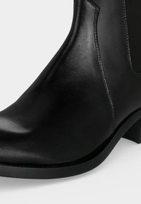 Bottine noire en cuir avec un petit talon et un panneau latéral élastique, présentée en gros plan de face et de côté.