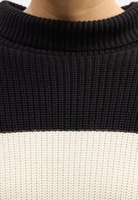 Gros plan d'un pull épais tricoté noir et blanc avec un col rond côtelé noir.