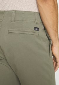 Olivgrüne Hosen aus Baumwollmischung, mit einer Rückentasche mit einem dunklen Logo-Patch, schmalem Schnitt, flachen Nähten und einer glatten Textur.