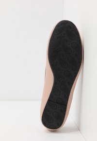 Semelle noire à motif d'une chaussure avec une tige beige lisse. La semelle présente un design paisley, ajoutant de la texture et de l'adhérence.