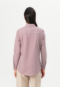 Long-sleeve shirt with red and white vertical stripes, collar, and buttoned cuffs, featuring a rounded hem and soft fabric texture.