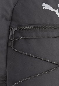 Zwarte rugzak met een ritssluiting, voorzien van elastische koorddetails en een Puma-logo aan de voorkant, gemaakt van duurzaam materiaal.