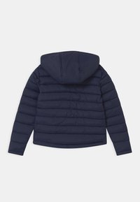 Marineblå pufferjakke med hætte, der har et quiltet design, glat tekstur og elastiske manchetter. Bagudsigten viser horisontale syninger.