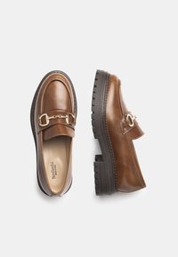 Mocassins en cuir marron avec une boucle dorée, bout rond et semelle en caoutchouc noir épaisse et texturée. Dessus lisse avec des coutures subtiles.