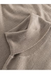 Hellbrauner, gestrickter Pullover mit hohem, umgeschlagenem Kragen. Glatte Textur mit gerippten Akzenten am Kragen und den Bündchen.