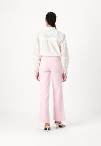 Valge broderie anglaise'iga pluus puffi varrukatega, millele on paari pandud roosa triibuline laia lõikega püksid ja madala kontsaga sandaalid, nähtud tagant.