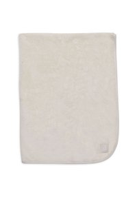 Zachte, beige pluche deken met een gladde textuur, afgeronde hoeken en een klein merklabel in de rechter benedenhoek.