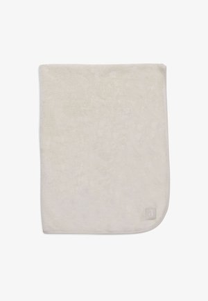 Weiche, beigefarbene Plüschdecke mit glatter Textur, abgerundeten Ecken und einem kleinen Markenetikett in der unteren rechten Ecke.