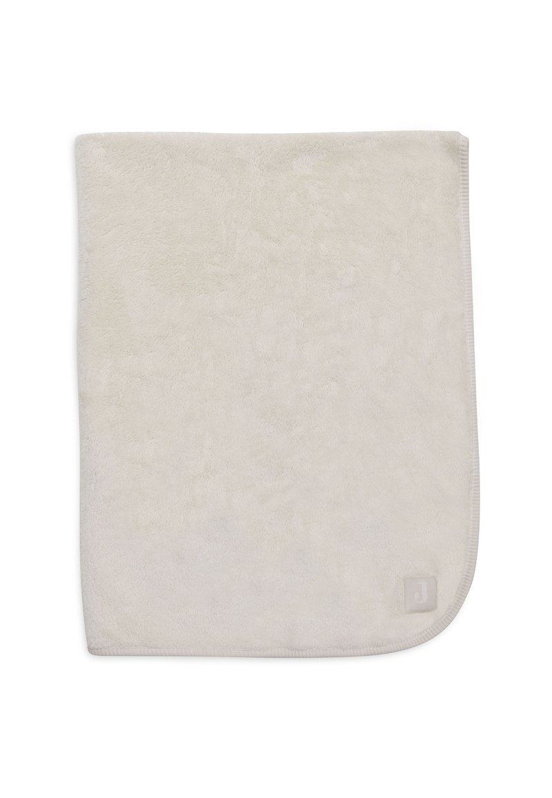 Zachte, beige pluche deken met een gladde textuur, afgeronde hoeken en een klein merklabel in de rechter benedenhoek.