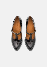Chaussures noires en cuir verni avec un design à lanière en T, bout pointu et perforations décoratives. Doublure intérieure marron et matériel de boucle.