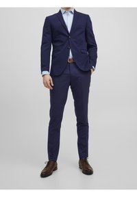 Námořnický oblek s přizpůsobeným sakem a slim-fit kalhotami, doplněný světle modrou košilí a hnědými koženými botami. Obsahuje dva knoflíky a kapsy.