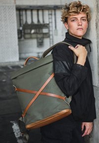 Grüner Rolltop-Rucksack aus strapazierfähigem Material, mit braunen Lederträgern und -akzenten, einer strukturierten Form und lässigem Design.