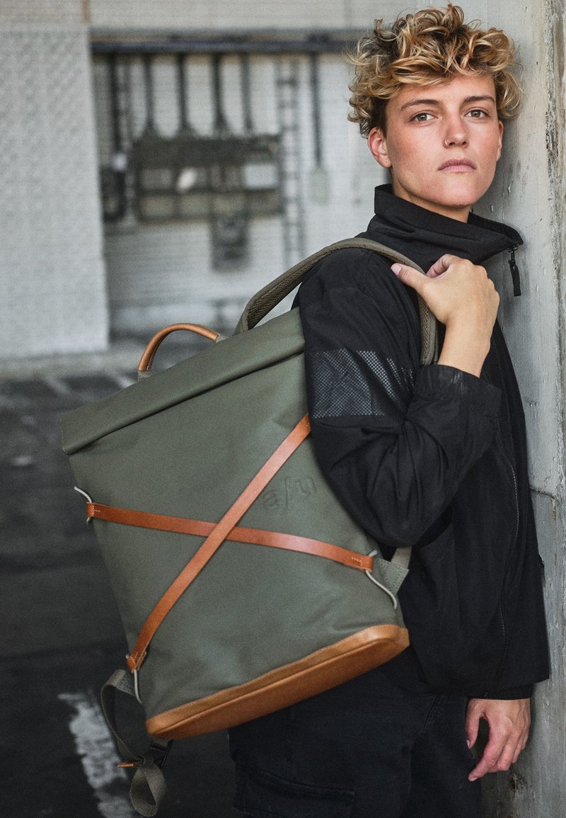 Grüner Rolltop-Rucksack aus strapazierfähigem Material, mit braunen Lederträgern und -akzenten, einer strukturierten Form und lässigem Design.