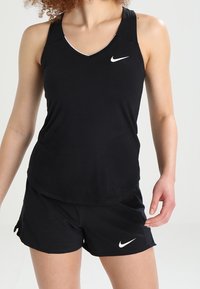 Camiseta deportiva negra de Nike con un diseño de cuello en V, que presenta un logo blanco, acompañada de pantalones cortos negros. Textura suave y tela ligera.