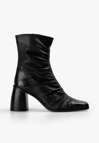 Bota de tobillo de cuero negro con diseño fruncido, punta puntiaguda y tacón grueso de bloque. Textura lisa con detalles mínimos.