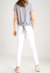 Grå kortärmad skjorta med knut på ryggen, i kombination med vita tajta byxor och ljusrosa sneakers. Slätt tyg med en avslappnad stil.