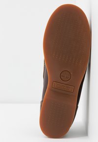 Braune Gummisohle mit rutschfester Struktur, mit Timberland-Logo. Die Seitenansicht zeigt eine gerade Kante und ein Obermaterial aus braunem Leder.