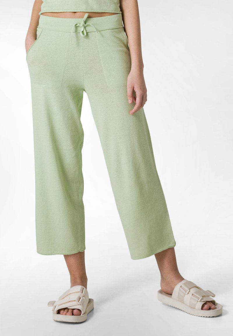 Pantaloni cropped verde chiaro realizzati in tessuto morbido, dotati di vita con coulisse, tasche laterali e una vestibilità rilassata. Abbinati a sandali beige con fascia.