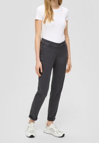 Pantalons en coton mélangé gris avec une coupe ajustée, présentant une fermeture à bouton et à glissière, des passants de ceinture et des ourlets roulés. Associés à un t-shirt blanc et des baskets.