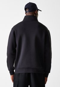 Schwarzer Pullover mit hohem Kragen, gerippten Bündchen und Saum. Verfügt über einen glatten Stoff und minimalistisches Design. Wird mit einer passenden Mütze getragen.