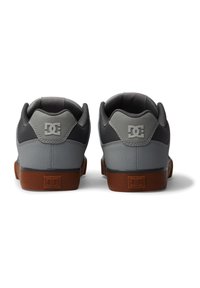 Scarpe da skate grigie con finitura testurizzata, colli imbottiti e suole in gomma marroni. Presentano il logo DC su entrambi i talloni.