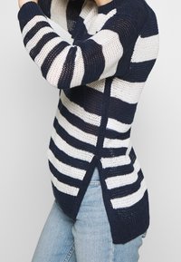 Navy and white striped knitted sweater featuring a relaxed fit, side slits, and textured fabric for breathability.
