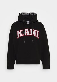 Černá mikina s kapucí, na které je velké bílé a červené logo "KANI" přes hrudník. Vyrobena z měkké tkaniny s ribkovanými manžetami.