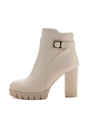 Beige Knöchelstiefel aus Kunstleder mit hohen Blockabsätzen, strukturiertem Sohlen, geschwungenem Design und einem Riemen mit einem metallischen Schnallendetail.