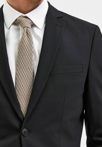 Svart dressjakke med en enkel knapp, sammen med en hvit skjorte og et vevet beige slips, som viser en glatt tekstur og rene linjer.