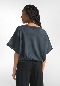 Top de manga corta gris oscuro con un ajuste holgado, escote barco y dobladillo fruncido. Cuenta con una pequeña etiqueta morada en la parte trasera.